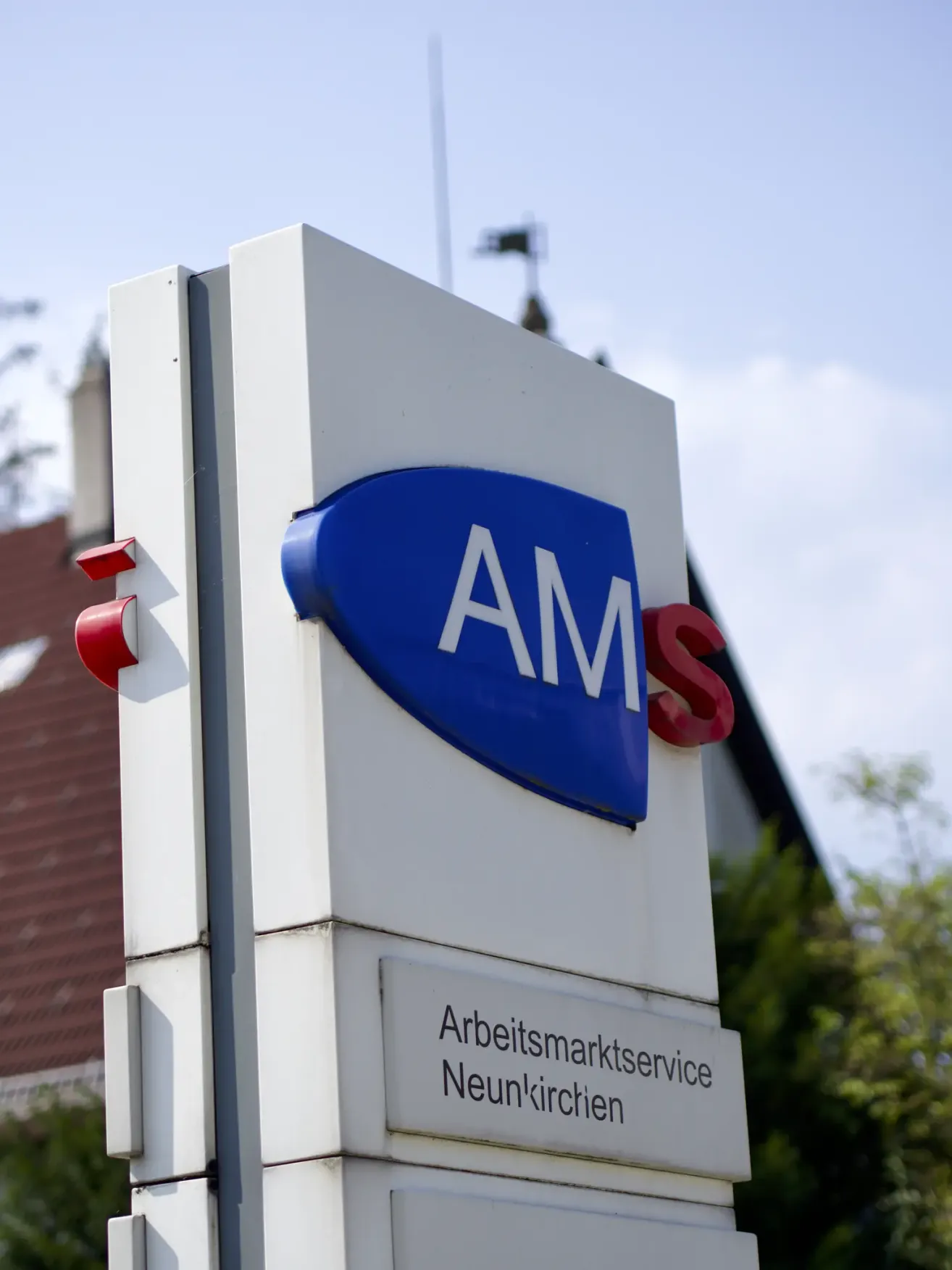 Ein blaues und weißes Schild mit den Buchstaben AMS in weißer Schrift auf weißem Hintergrund. Unten befindet sich ein weißes Schild mit schwarzem Text, das Arbeitsmarktservice Neunkirchen besagt.