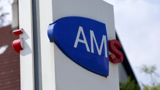 Ein blaues und weißes Schild mit den Buchstaben AMS in weißer Schrift auf weißem Hintergrund. Unten befindet sich ein weißes Schild mit schwarzem Text, das Arbeitsmarktservice Neunkirchen besagt.