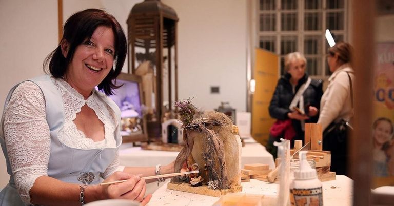 Eine Frau malt eine Skulptur eines Paares von Tieren, lächelt in einem Kunstatelier mit einer Holzlampe und einem Fenster.