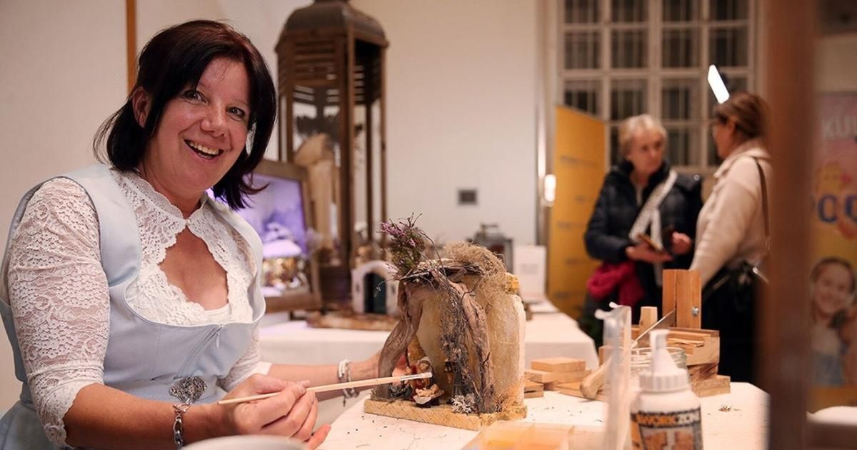 Eine Frau malt eine Skulptur eines Paares von Tieren, lächelt in einem Kunstatelier mit einer Holzlampe und einem Fenster.