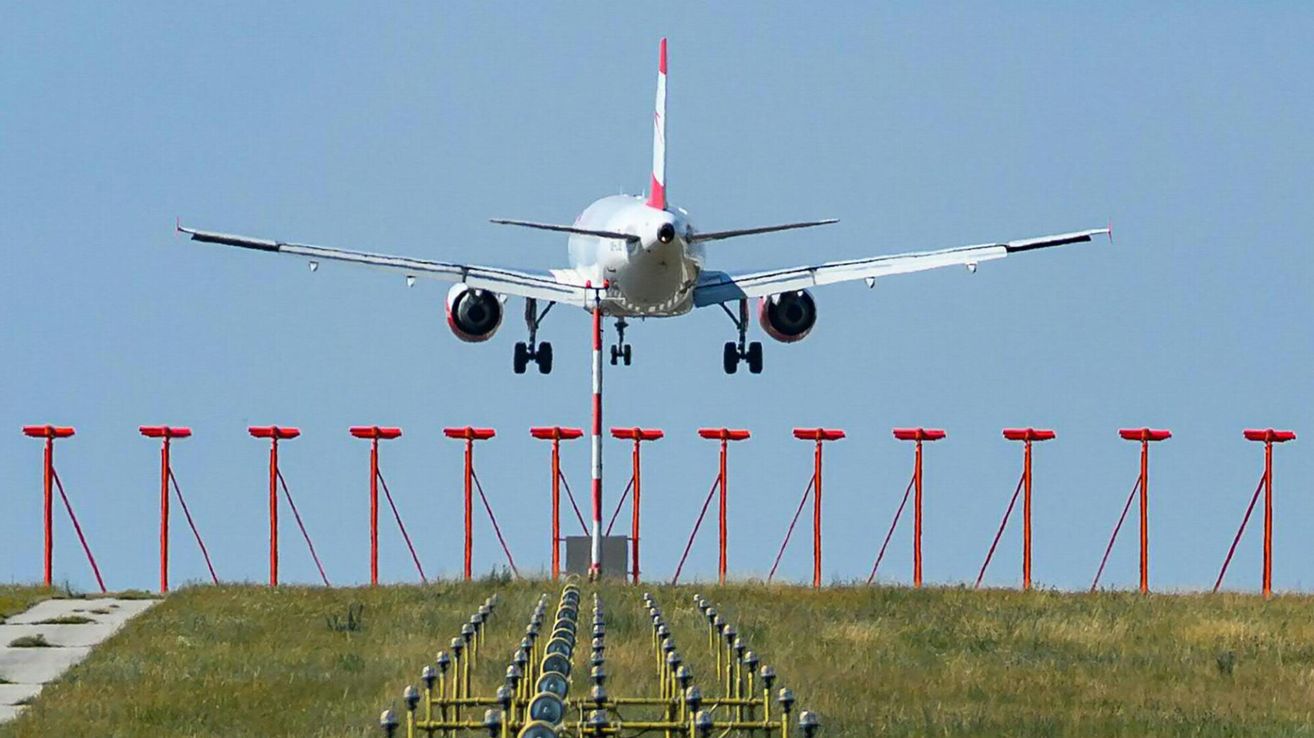Ein Flugzeug mit einer rot-weißen Heckflosse startet von einer Landebahn mit roten und weißen Markierungen auf dem Boden.