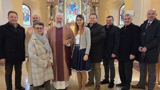 Eine Gruppe von Menschen, darunter eine Frau und ein Mann in religiöser Kleidung, stehen lächelnd in einer Kirche.
