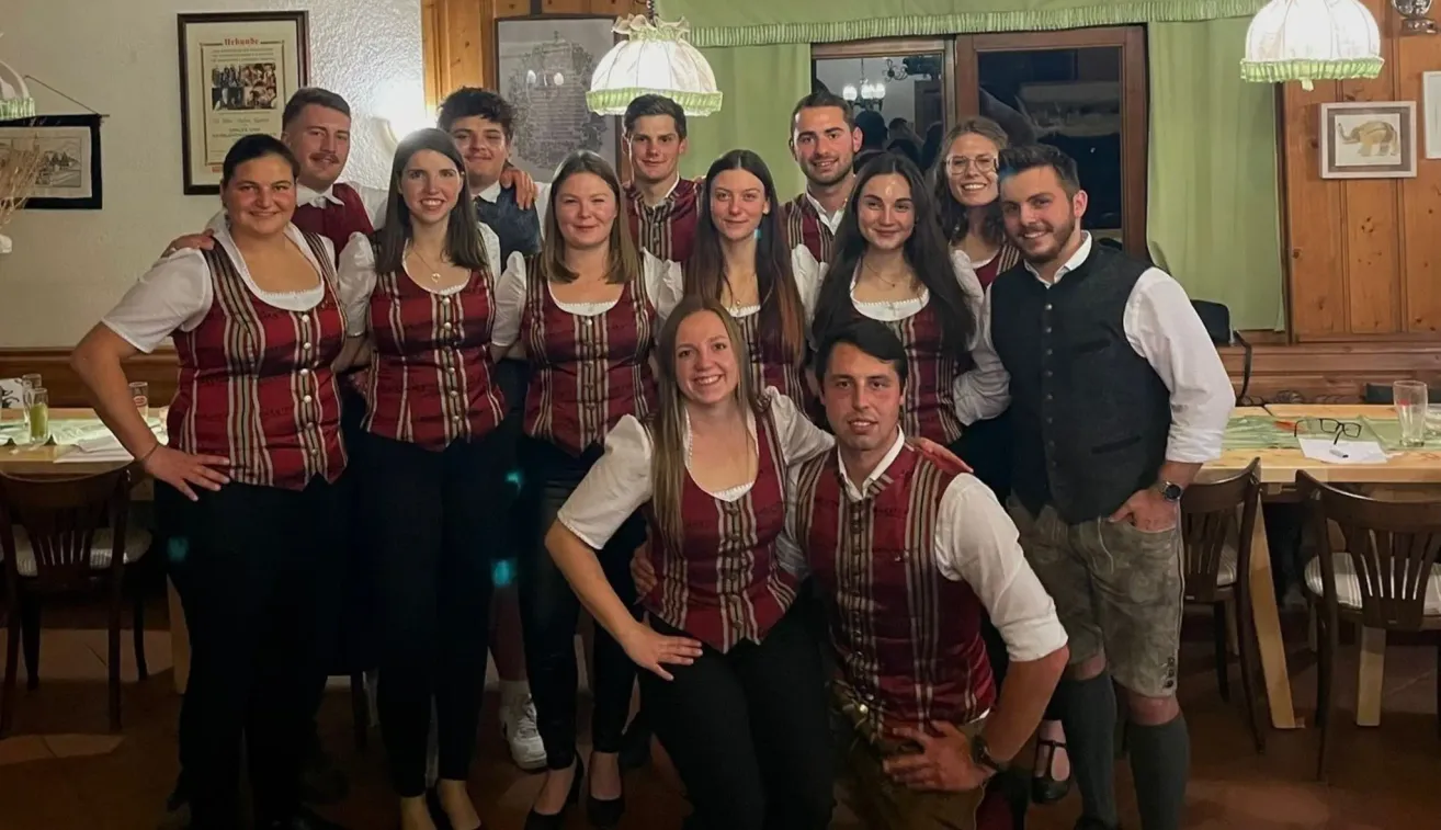 Eine Gruppe junger Menschen, die in traditioneller Kleidung posiert. Sie lächeln alle und stehen eng beieinander.