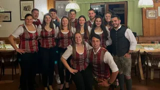 Eine Gruppe junger Menschen, die in traditioneller Kleidung posiert. Sie lächeln alle und stehen eng beieinander.
