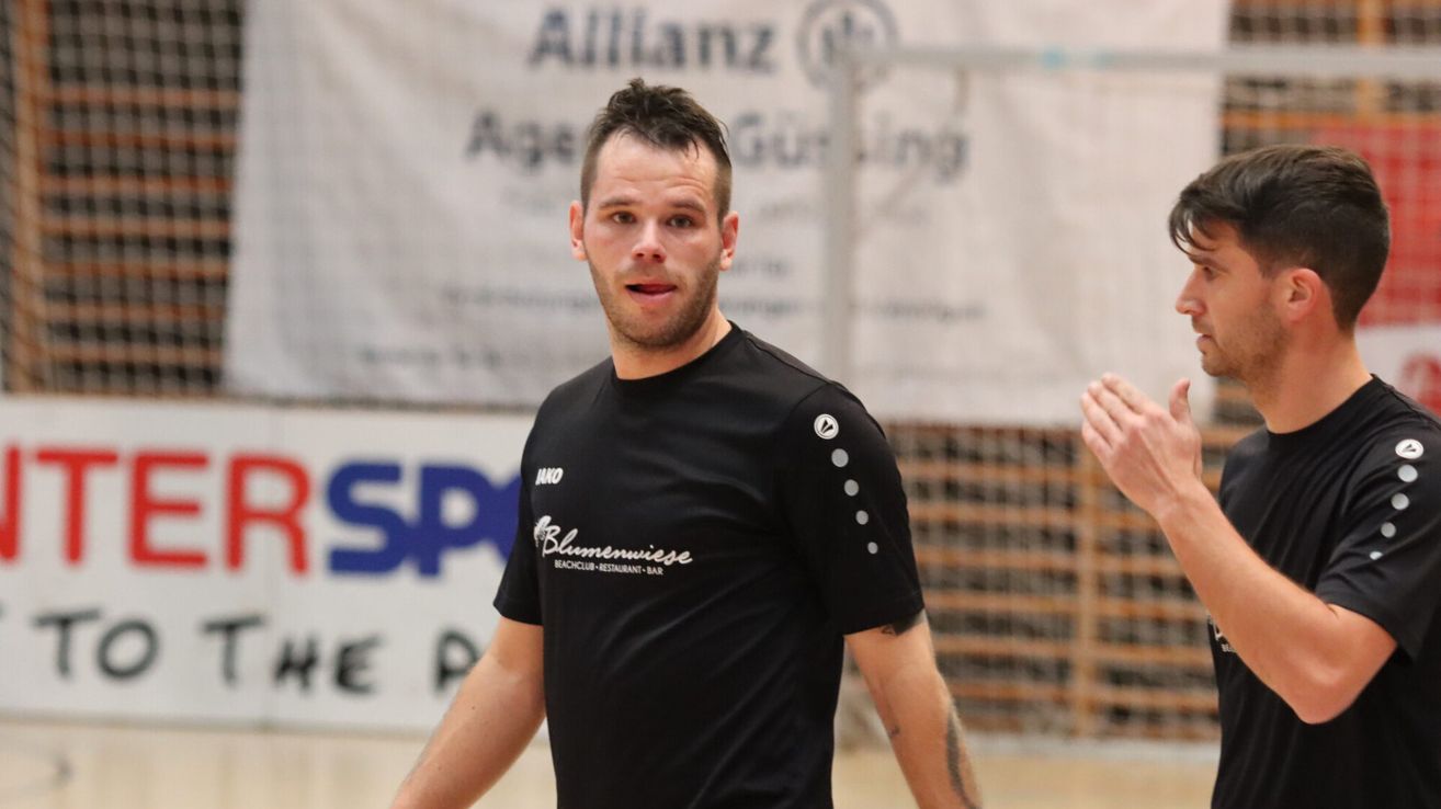 Ein Mann mit Tätowierungen am Arm trägt ein schwarzes Shirt mit weißen Buchstaben und läuft in einer Sporthalle.