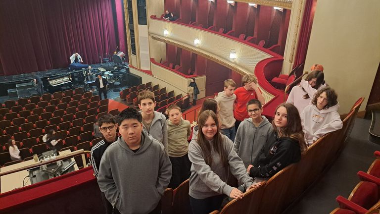 Eine Gruppe von Schülern in Hoodies steht in einem Theater mit leeren Sitzen vor einer Bühne.