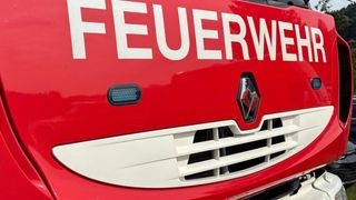 Nahaufnahme der Vorderseite eines roten Feuerwehrwagens, mit dem Wort 'FEUERWEHR' in Weiß, einem roten Renault-Logo und einem Lichtbalken auf der linken Seite.