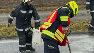 Zwei Feuerwehrleute in voller Ausrüstung gehen auf einer nassen Straße. Einer hält einen weißen Behälter, der andere benutzt einen Stock.
