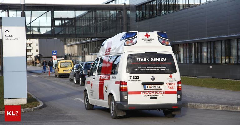 Ein weißer Krankenwagen mit roten Kreuzen fährt die Straße hinunter, im Hintergrund ein Gebäude. Auf der Rückseite des Krankenwagens steht "Stark Genug?" und hat ein rotes Kreuz auf der Heckklappe.