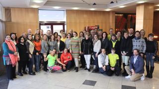 Eine Gruppe von Menschen in passenden farbigen Outfits posiert für ein Foto in einem Innenbereich. Einige lächeln, und einige stehen hinter der Person in der Mitte. Es gibt an der Decke montierte Lampen, und eine Coca-Cola-Maschine steht hinter ihnen.