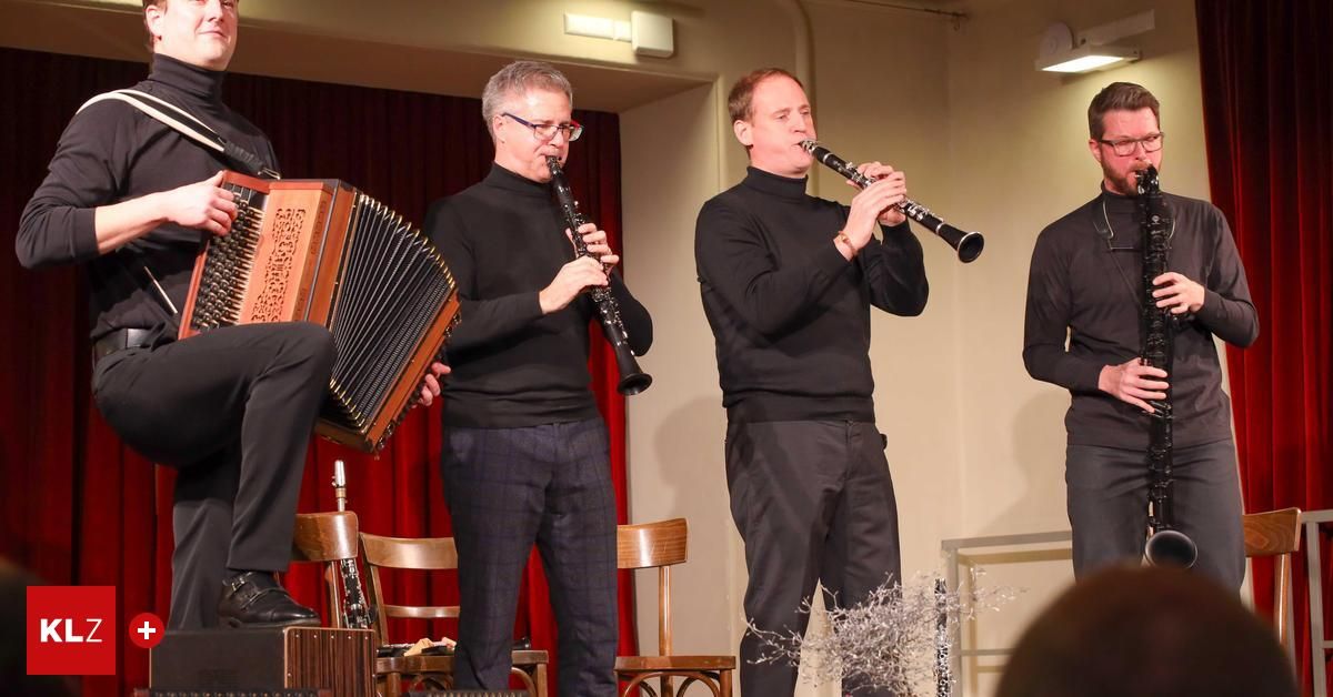 Drei Musiker treten auf der Bühne auf. Einer spielt Klarinette, der andere Akkordeon und der dritte ebenfalls Klarinette. Dahinter befindet sich ein roter Vorhang und Holzstühle.