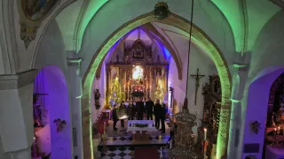 Eine Gruppe von Menschen versammelt sich in einer Kirche, geschmückt mit Kerzen und Weihnachtsdekorationen. Sie stehen vor einem Altar, möglicherweise an einer Zeremonie beteiligt.