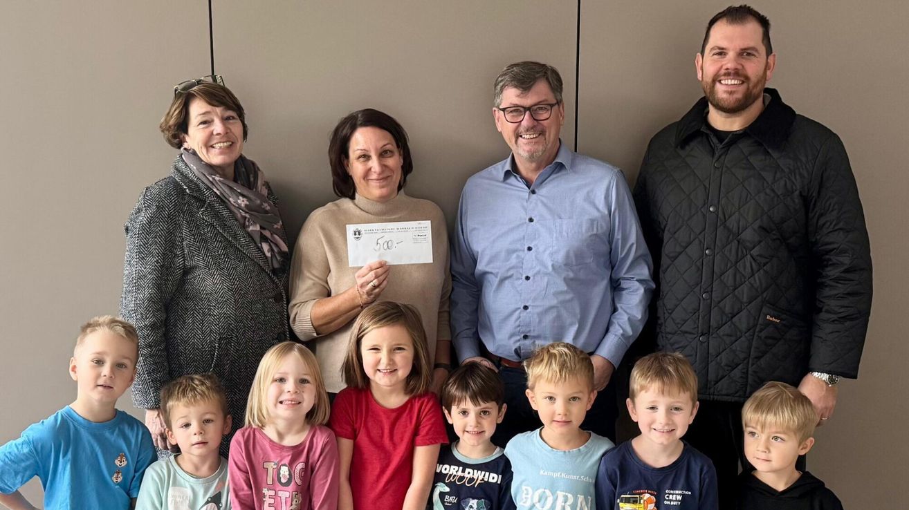 Eine Gruppe von Menschen steht lächelnd zusammen. Eine Frau hält einen Scheck mit der Nummer 500. Hinter ihr stehen zwei Erwachsene, einer mit einer Brille. Unten lächeln vier Kinder, eines in einem roten Shirt.