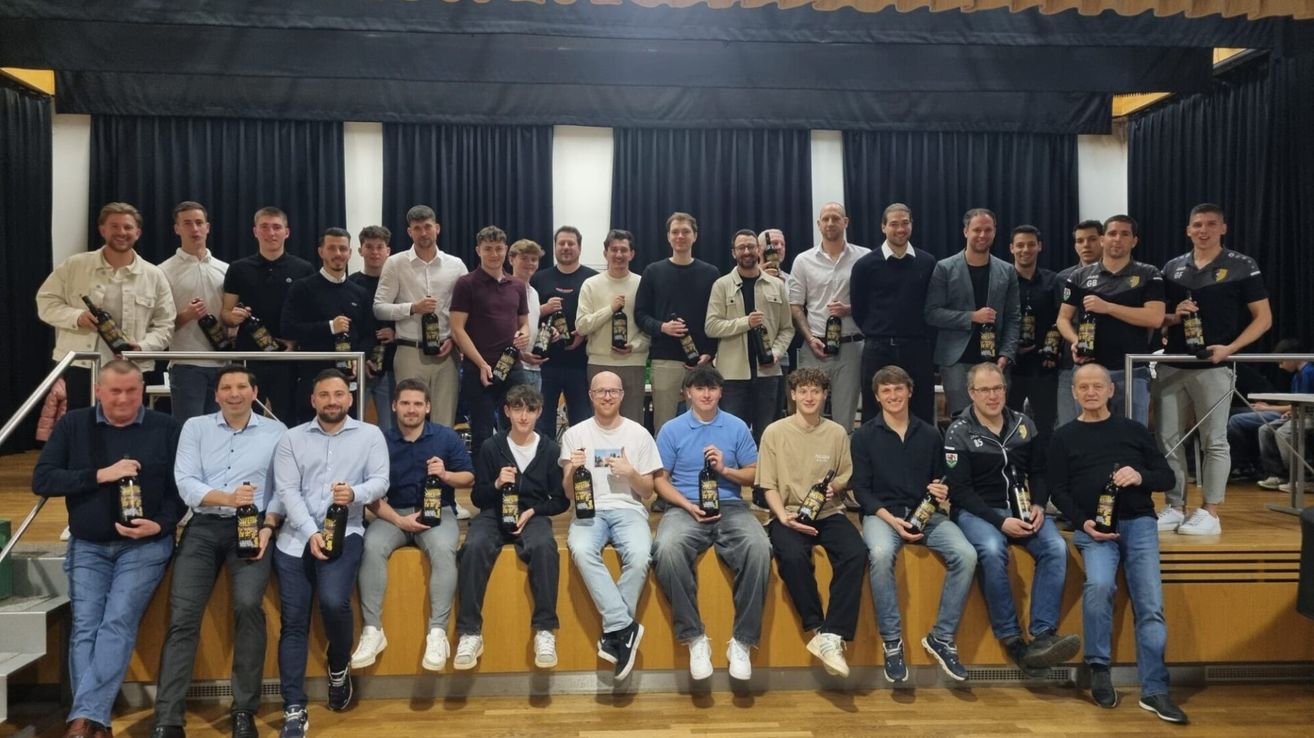 Eine Gruppe von Männern in unterschiedlicher Kleidung hält Flaschen und sitzt oder steht auf einer Holzbank mit Vorhanghintergrund.