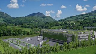 Ein Luftbild eines großen Gebäudes mit grünem Dach, umgeben von einer üppigen Landschaft mit Bergen, Grünflächen und geparkten Fahrzeugen.