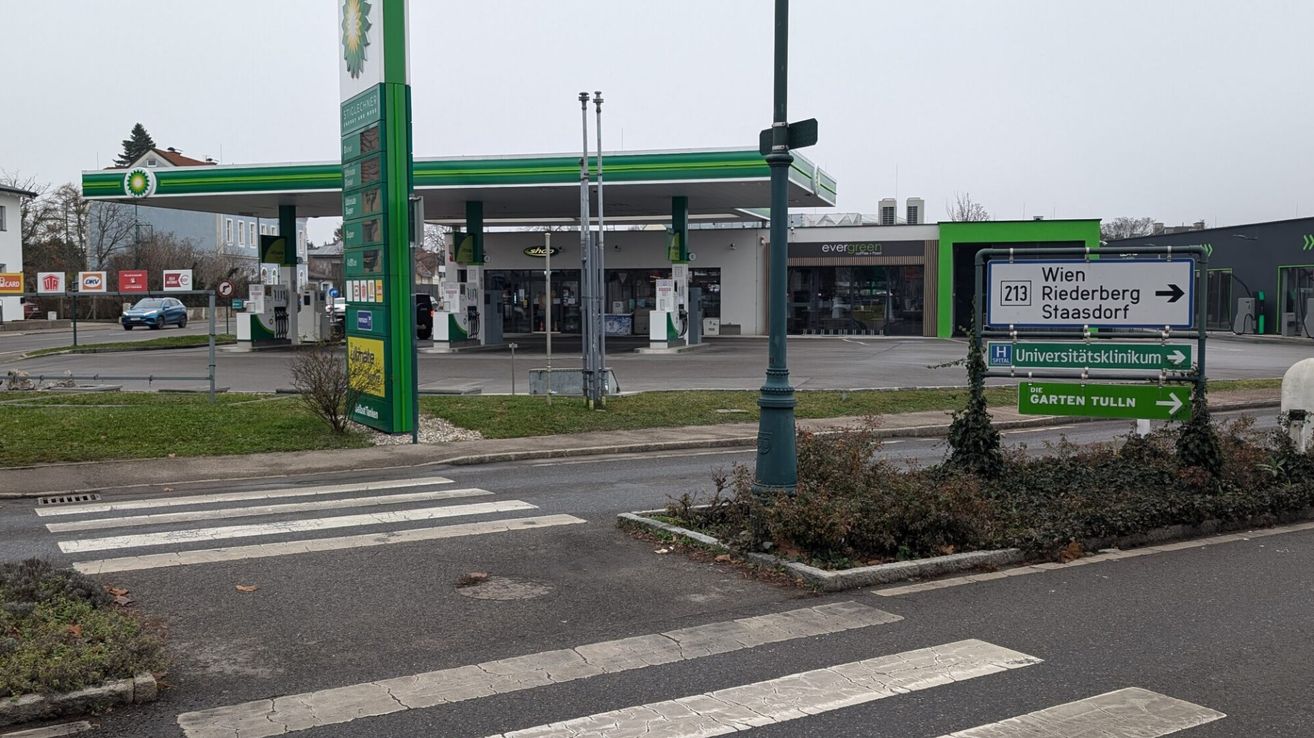 Eine BP-Tankstelle mit einem Geschäft an der Seite, in der Nähe eines Zebrastreifens mit einem Fußgängerzeichen. Die Tankstelle hat ein grünes Vordach und das Geschäft hat Glasfenster.