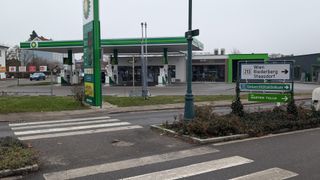 Eine BP-Tankstelle mit einem Geschäft an der Seite, in der Nähe eines Zebrastreifens mit einem Fußgängerzeichen. Die Tankstelle hat ein grünes Vordach und das Geschäft hat Glasfenster.