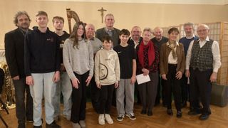 Eine Gruppe von Menschen, darunter Erwachsene und Kinder, posiert für ein Foto in einer Kirche. Ein Kreuz befindet sich an der Wand hinter ihnen.