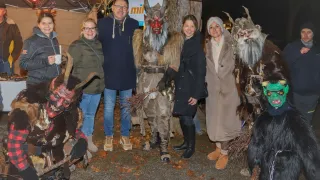 Eine Gruppe von Menschen in Kostümen, einer mit einer hörnerbesetzten Dämonenmaske, steht in einer nächtlichen Außenumgebung. Es gibt Blätter auf dem Boden, und sie posieren für ein Foto.