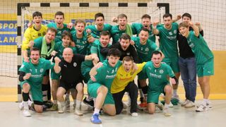 Eine Gruppe junger Männer in grünen und gelben Trikots feiert in einer Turnhalle und posiert für ein Foto vor einem Volleyballnetz.