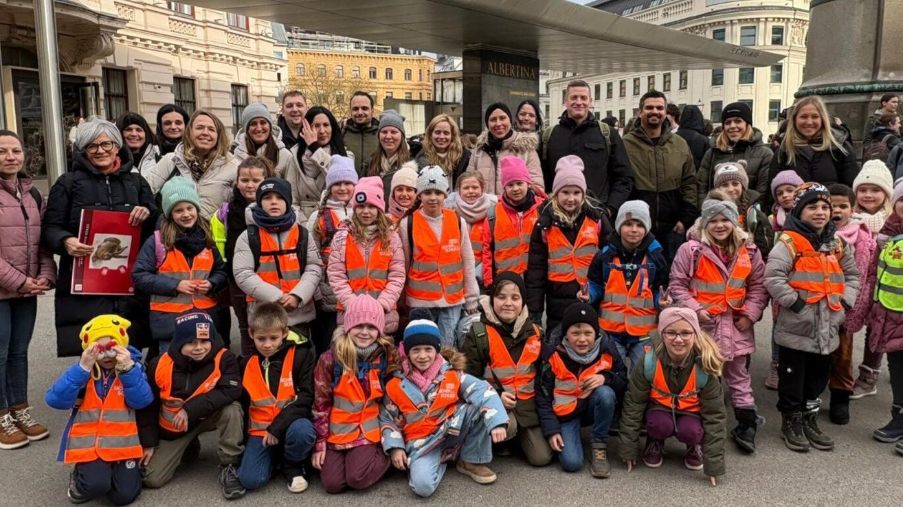 Eine Gruppe von Kindern und Erwachsenen in orangenen Westen posiert für ein Foto vor Gebäuden.