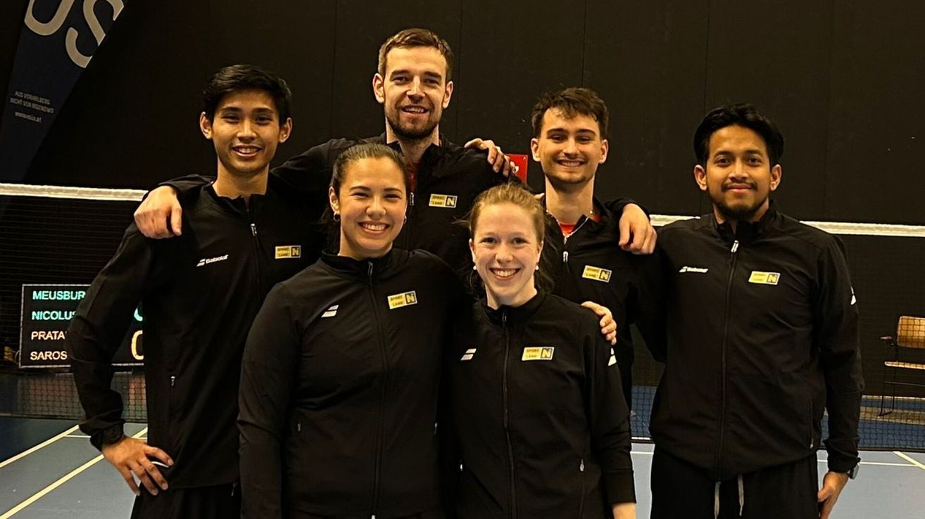 Eine Gruppe von Athleten in schwarzen Jacken mit gelben Logos posiert für ein Foto auf einem Platz.