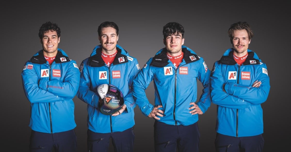 Vier männliche Athleten in blauen Skijacken mit dem Buchstaben A und der Nummer 1 auf ihren Jacken. Einer hält einen Helm.
