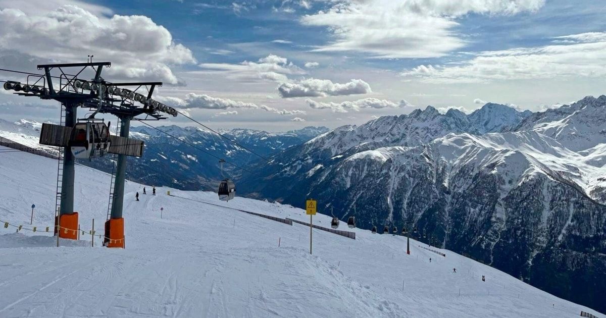 Eine Skilift fährt über eine verschneite Berglandschaft unter einem teilweise bewölkten Himmel.