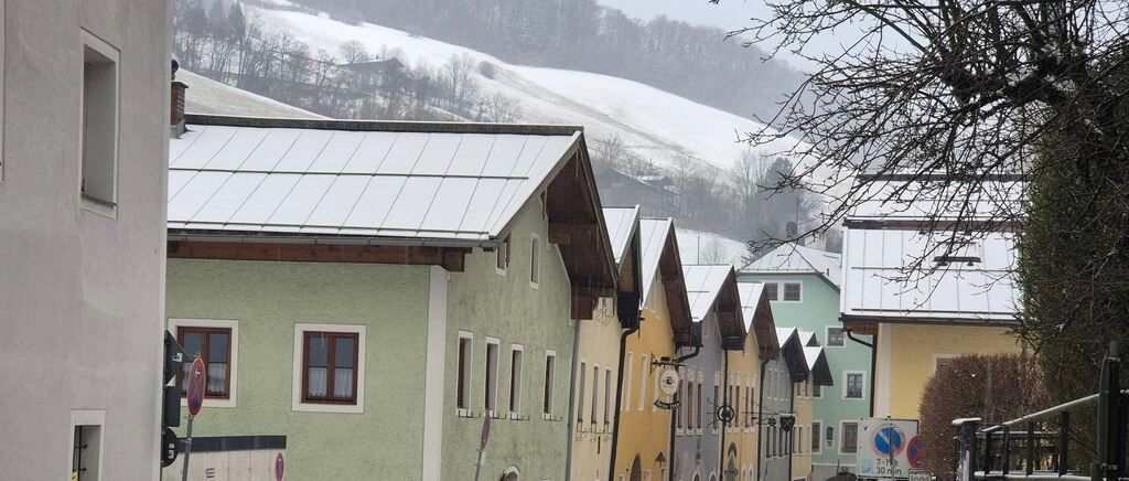 Eine Reihe farbenfroher Häuser mit schneebedeckten Dächern auf einer Straße. Ein schneebedeckter Hügel im Hintergrund.