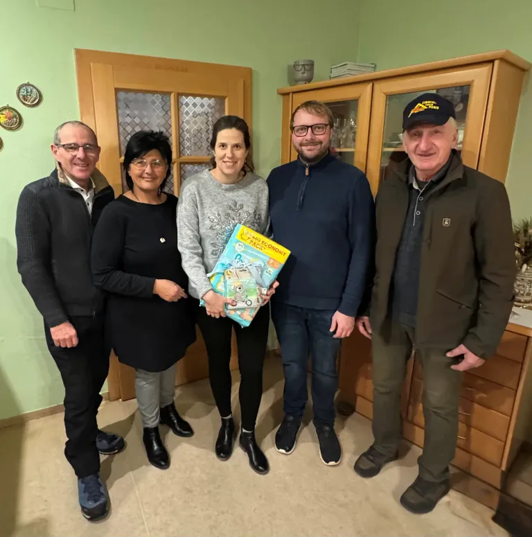 Fünf Erwachsene stehen in einem Raum und lächeln für ein Foto. Eine Frau hält ein Buch mit dem Titel 'Play Economy'. Hinter ihnen stehen Holzschränke und eine Tür.