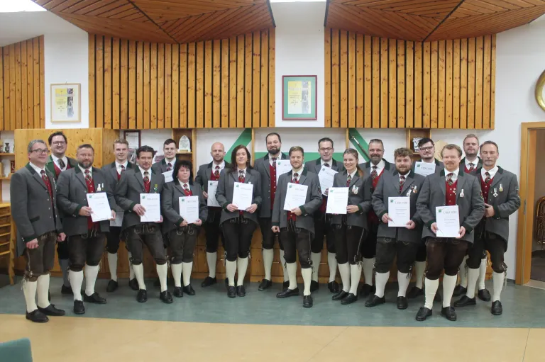Eine Gruppe von Menschen in traditioneller Kleidung, möglicherweise für eine formelle Veranstaltung, posiert für ein Foto in einem Raum mit Holzwänden und Regalen.