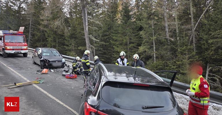 Einsatzkräfte arbeiten an einem Autounfall auf einer Straße mit Bäumen und Leitplanke. Die Fahrzeuge sind zerstört, und die Einsatzkräfte tragen Helme und Uniformen.