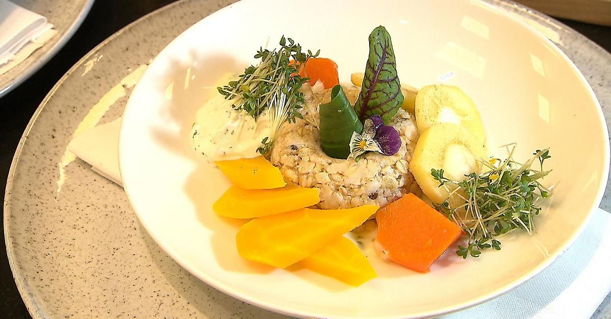 Ein weißer Teller mit einem Gericht aus Reis, garniert mit verschiedenen Gemüsesorten und Kräutern, und gekrönt mit einer kleinen Blume.