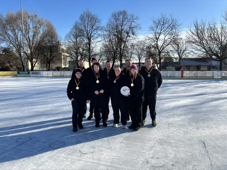 Eine Gruppe von Menschen in Winterkleidung posiert für ein Foto auf einer Eisbahn mit Medaillen um den Hals.