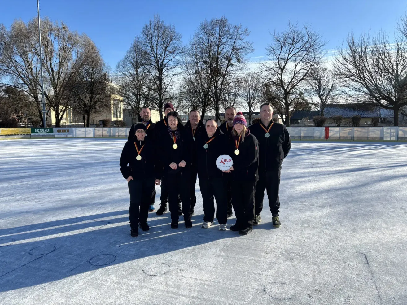 Eine Gruppe von Menschen in Winterkleidung posiert für ein Foto auf einer Eisbahn mit Medaillen um den Hals.
