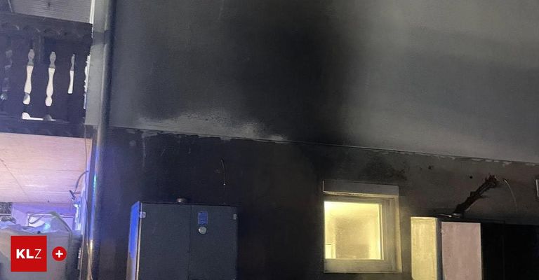 Ein dunkler Raum mit rußigen Wänden und einem beleuchteten Fenster. Ein Metallkasten mit blauem Licht steht links.