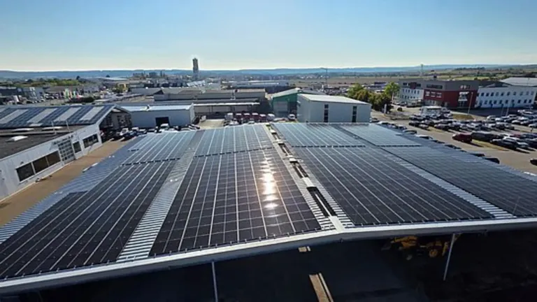 Eine Luftaufnahme eines großen Industriegebiets mit Solarmodulen auf den Dächern und Gebäuden. In der Nähe sind Fahrzeuge geparkt.