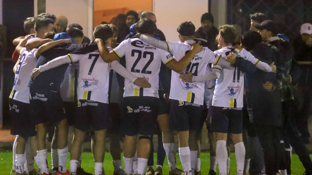 Eine Gruppe von Athleten, die weiße Trikots mit Nummern tragen, versammelt sich auf einem Feld bei Nacht. Sie sind von anderen Menschen umgeben.