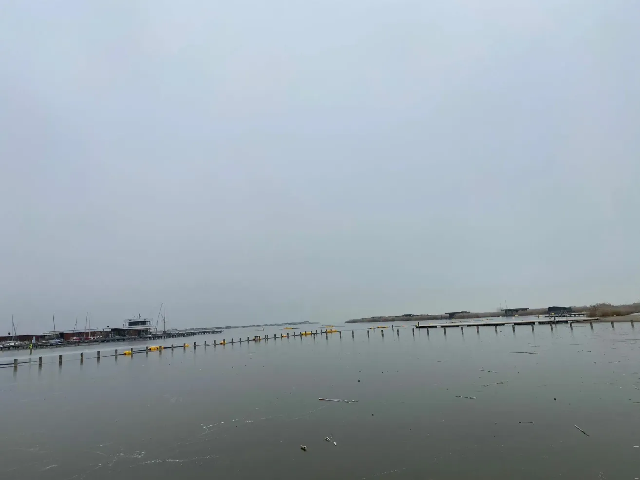 Ein riesiges Gewässer mit einem bewölkten Himmel, einem Dock mit vielen Stangen und einem Gebäude in der Ferne.