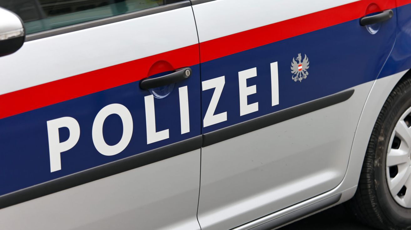 Nahaufnahme der Tür eines Polizeiwagens mit dem Wort 'POLIZEI' in Weiß auf blauem Hintergrund, mit einem Logo, das einen Adler auf einem roten Streifen zeigt.