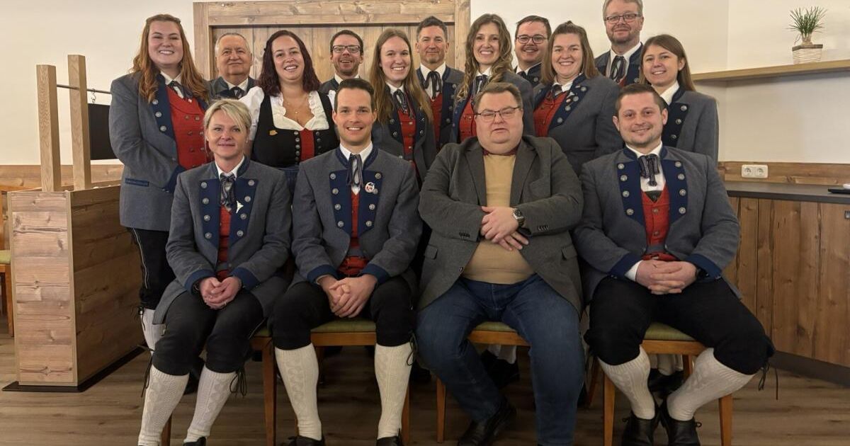 Eine Gruppe von Menschen in traditionellen Kostümen sitzt in Reihen. Sie scheinen für ein Foto zu posieren. Sie tragen weiße Socken und Lederschuhe.