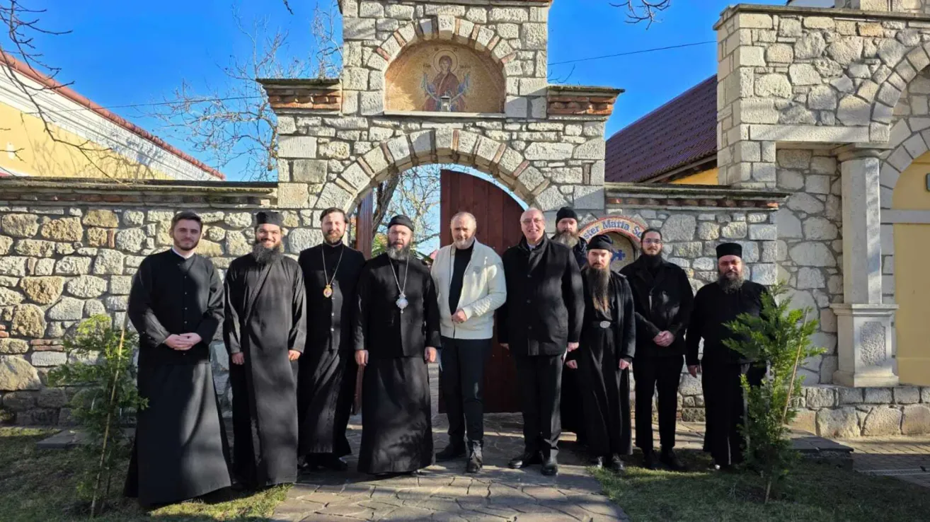 Eine Gruppe von Männern, einige in schwarzen Roben und andere in Anzügen, posiert für ein Foto vor einem steinernen Torbogen.