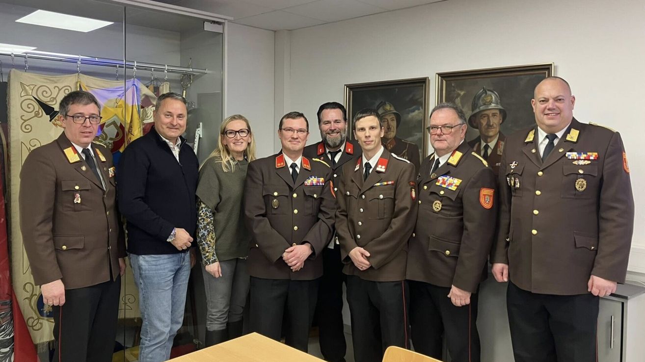 Eine Gruppe von Militärangehörigen und Zivilisten posiert für ein Foto in einem Büro mit zwei gerahmten Porträts an der Wand.