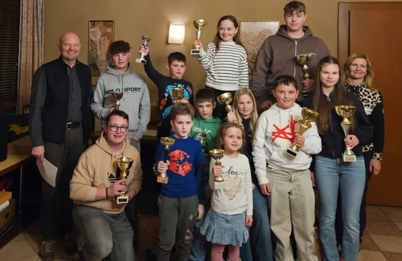 Eine Gruppe von Kindern und Erwachsenen posiert für ein Foto mit Pokalen in der Hand. Sie lächeln und scheinen eine Leistung zu feiern.