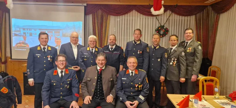 Gruppe von Männern in Uniformen, zwei sitzend und andere stehend, posieren für ein Foto mit einem Weihnachtskranz und einem Weihnachtsmannhut im Hintergrund.