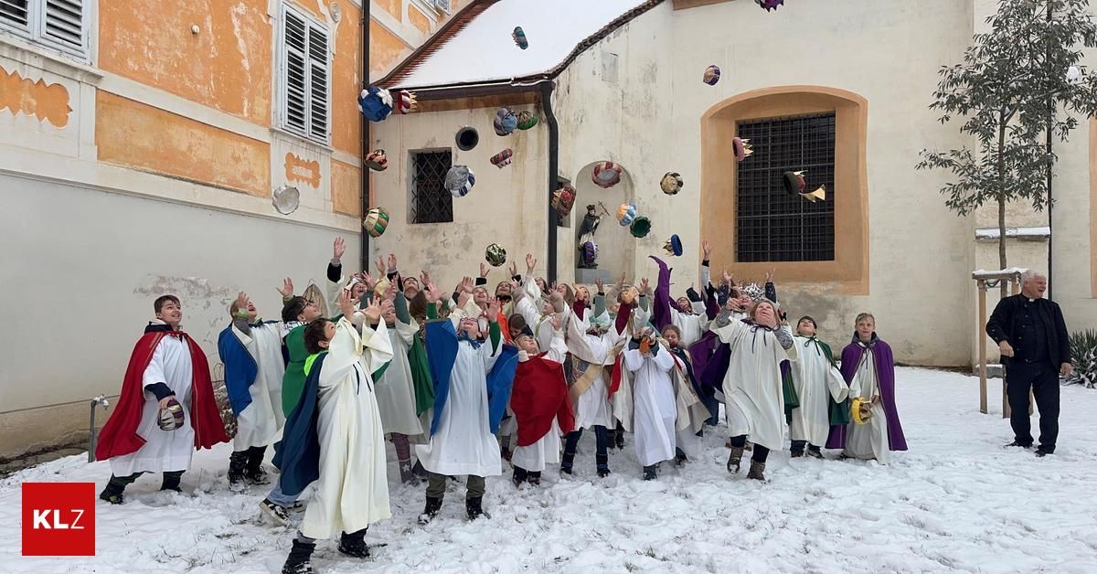 Eine Gruppe von Kindern in verschiedenen farbigen Gewändern wirft bunte Gegenstände vor einem Gebäude in die Luft.