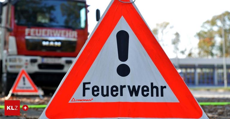 Ein Warnzeichen für Feuerwehrleute mit einem Ausrufezeichen in der Mitte. Ein roter Feuerwehrwagen ist im Hintergrund sichtbar.