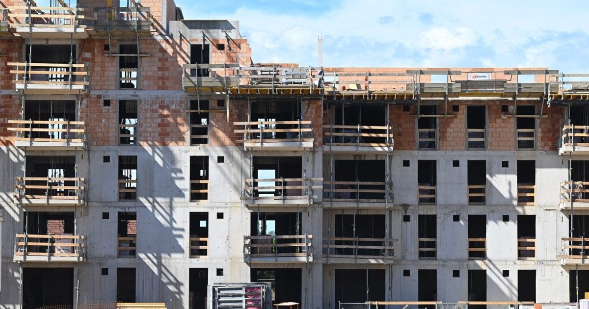 Ein im Bau befindliches Gebäude mit mehreren Stockwerken und Balkonen. An den Seiten sind Gerüste aufgestellt, und Schatten fallen auf die Wände.