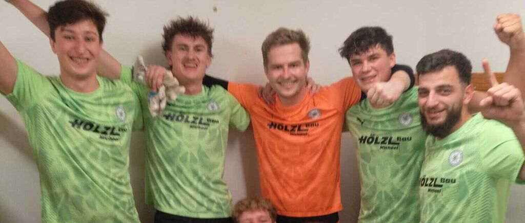 Eine Gruppe von Fußballspielern in grünen und orangefarbenen Trikots posiert lächelnd für ein Foto. Das Wort HOLZL ist auf der Vorderseite ihrer Trikots aufgedruckt.