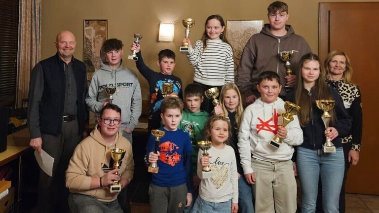 Eine Gruppe von Kindern und Jugendlichen, die goldene Pokale halten, lächeln und posieren für ein Foto in einem Raum.